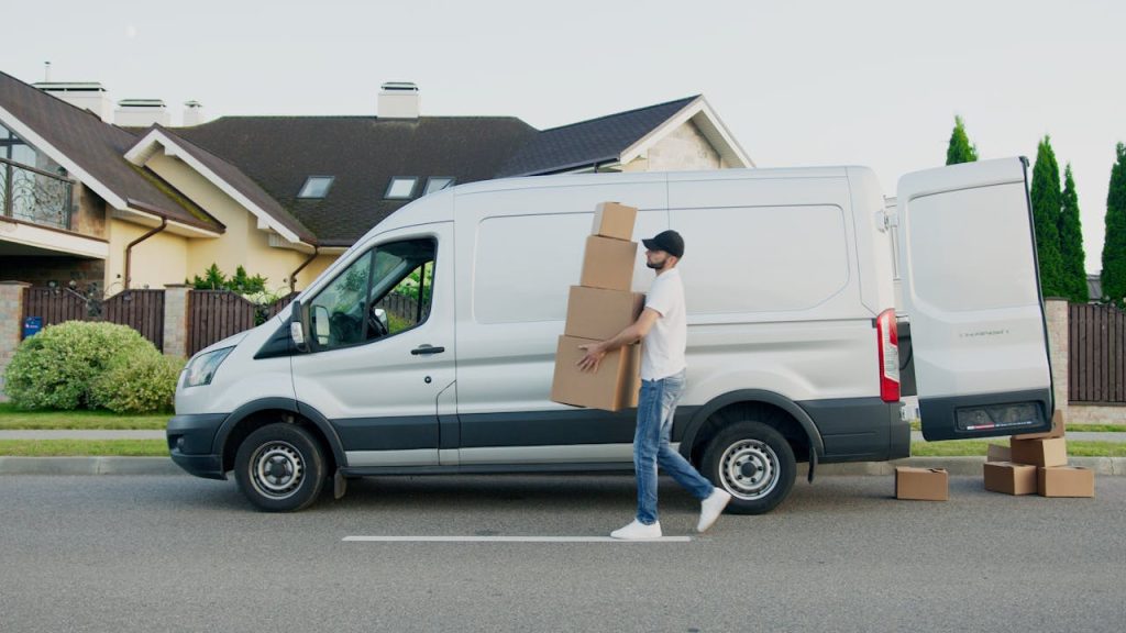 pexels photo 5025669 Man unloading cardboard boxes from a delivery van in a suburban neighborhood street.
