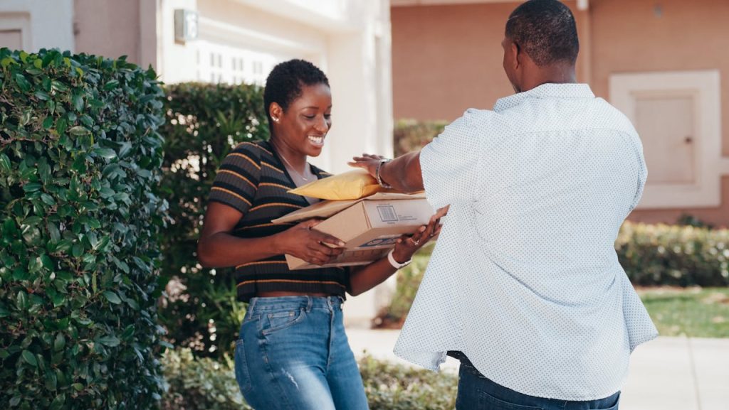 pexels photo 6869055 A smiling woman receives multiple packages from a delivery man outdoors.